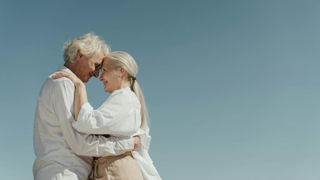 Senior couple embracing outdoors, depicting love and happiness against a clear blue sky.