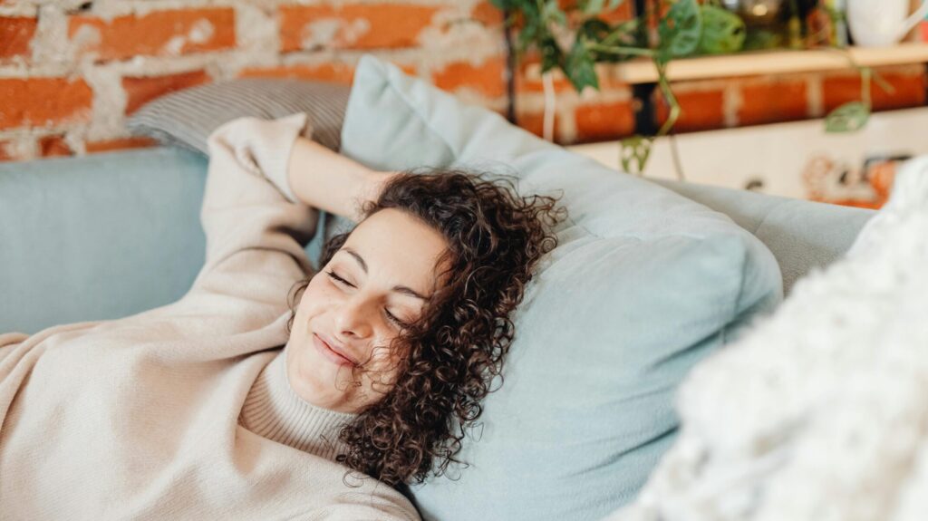 Woman with curly hair relaxing on a comfortable sofa in a cozy indoor setting.